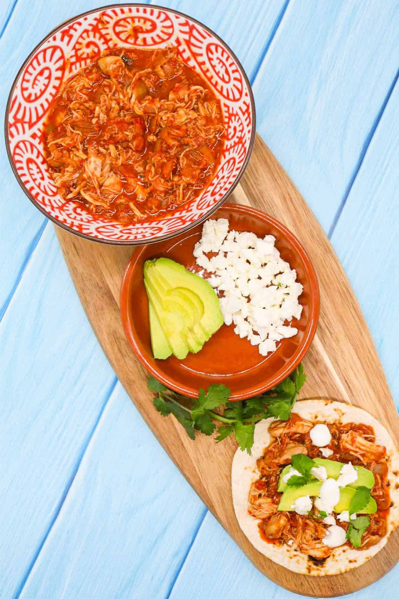 Chicken tinga on flour tortilla with avocado and cheese on wooden board