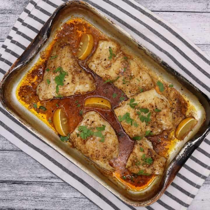 Baked cajun garlic butter cod in roasting tray with lemon wedges