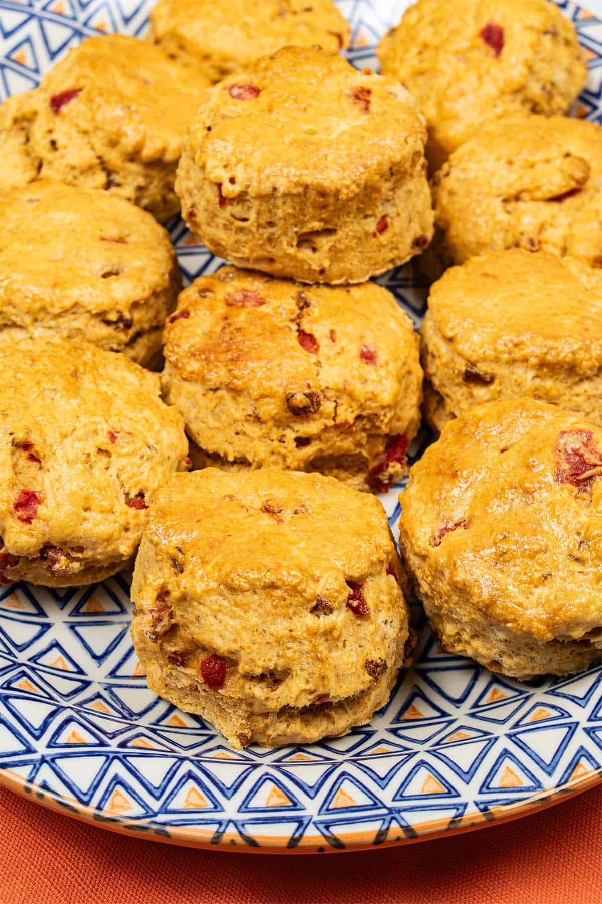 Close up of chorizo, red pepper and paprika scones on a blue and orange patterned platter on top of an orange napkin.