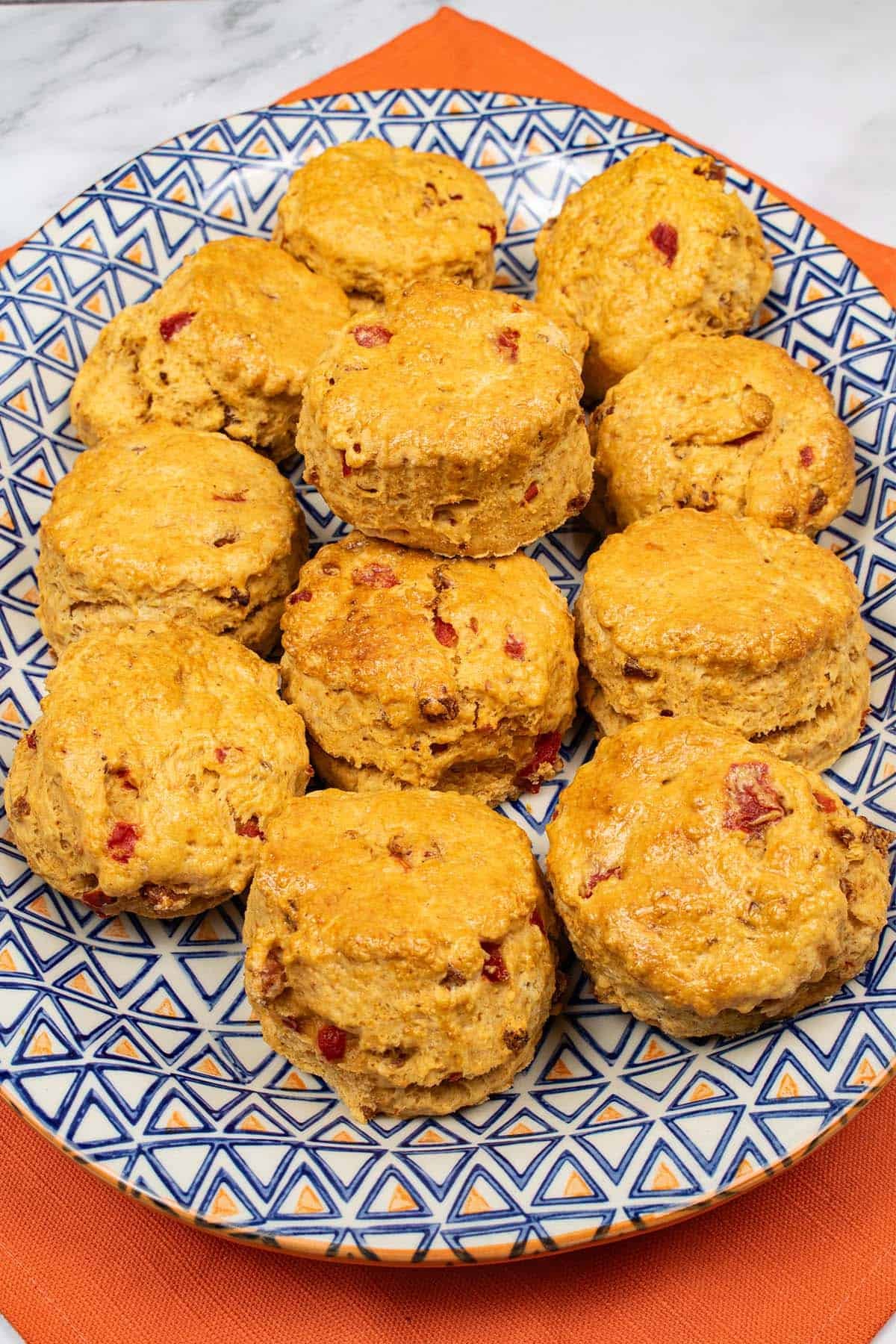 Chorizo, red pepper and paprika scones on a blue and orange patterned platter on top of an orange napkin.