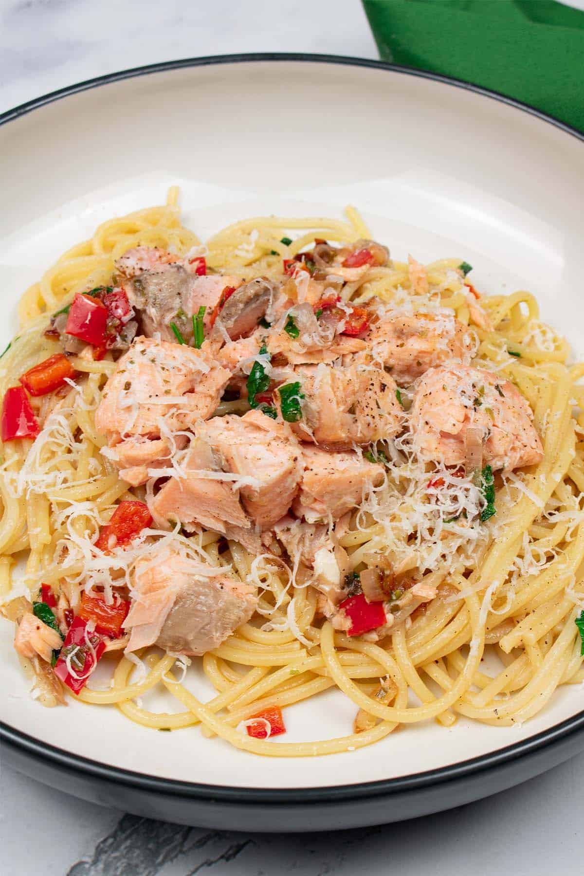 Spaghetti with hot smoked salmon, chilli and white wine in a black and cream bowl with a green napkin on the side.