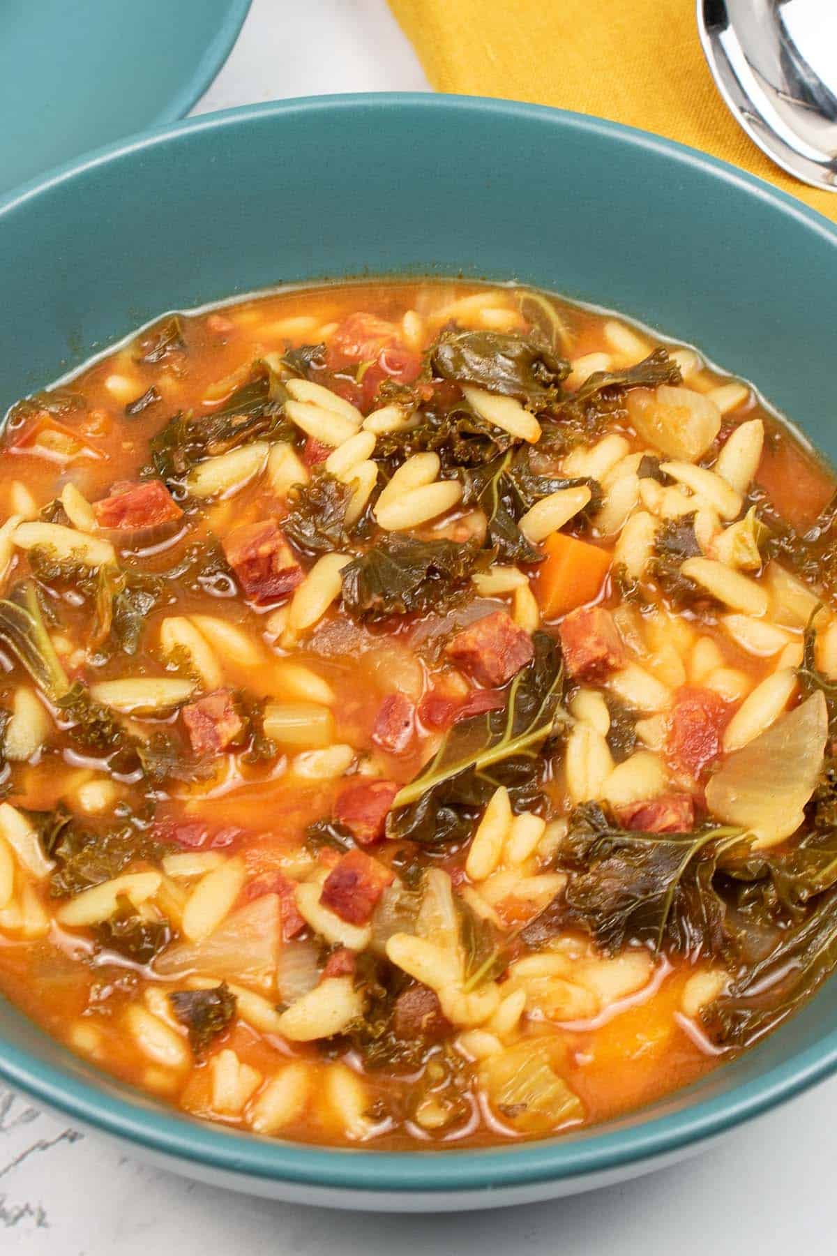 Close up of chorizo and orzo soup in a teal bowl.