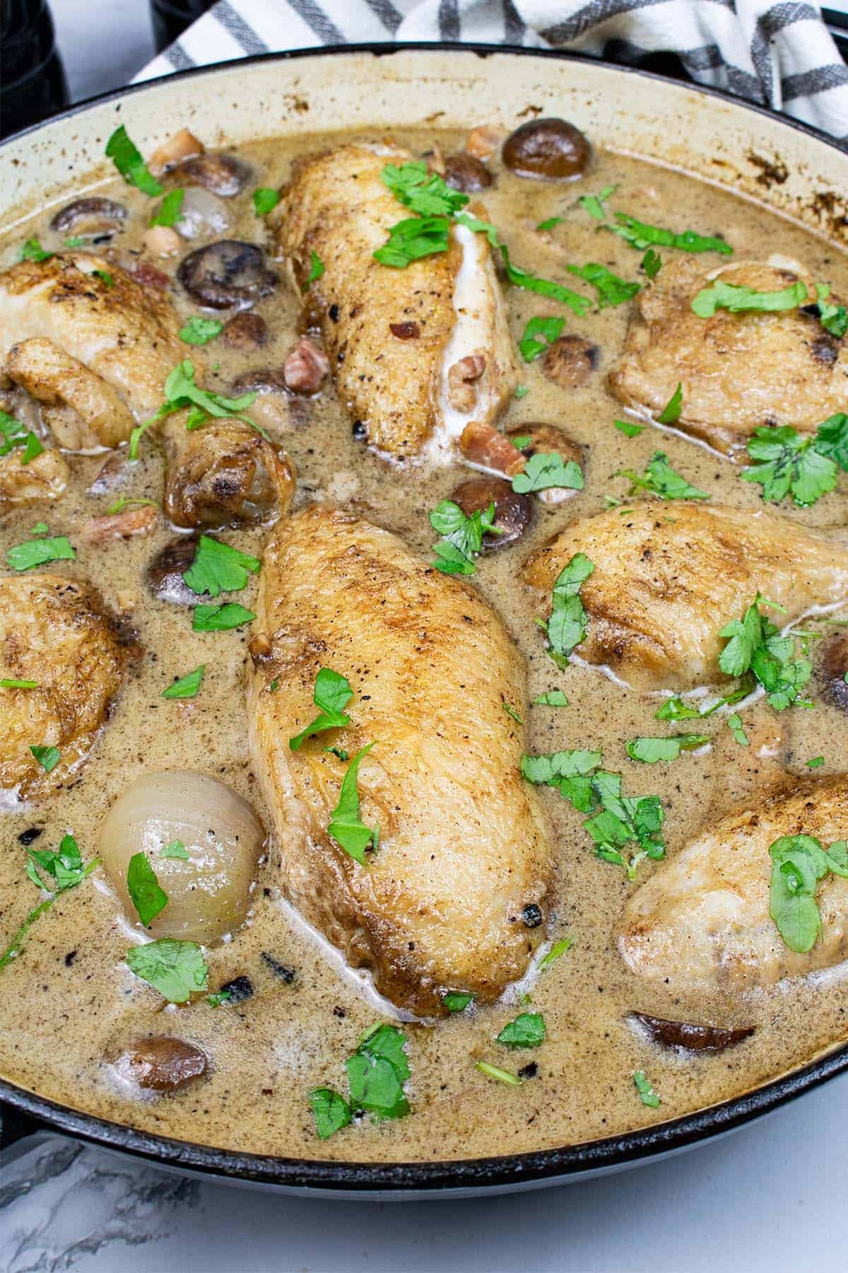 Coq au riesling in a round casserole with a black and white striped towel around the handles.