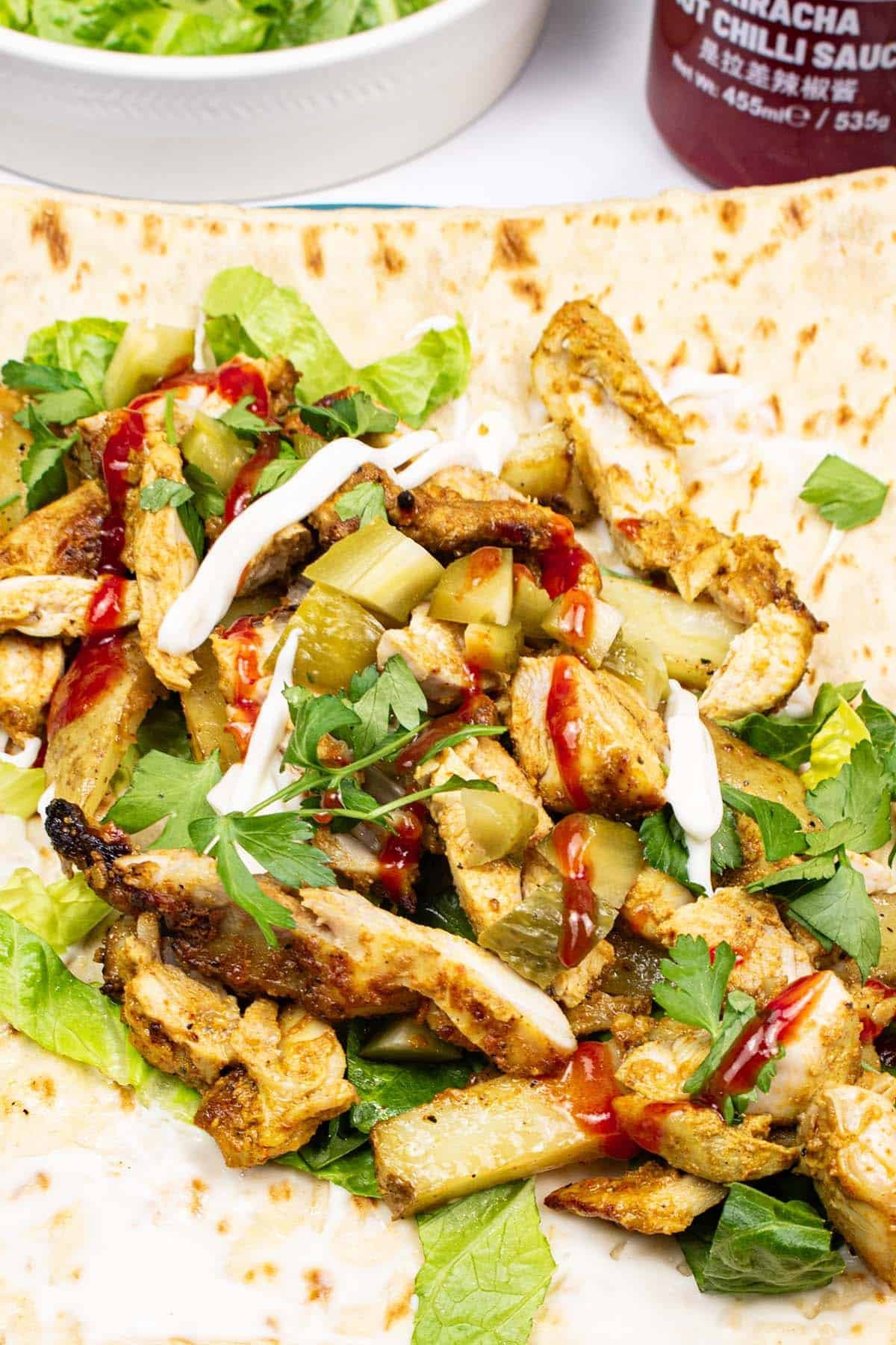 Close up of assembled kebab king shawarma with a dish of shredded lettuce and bottle of sriracha on the side.