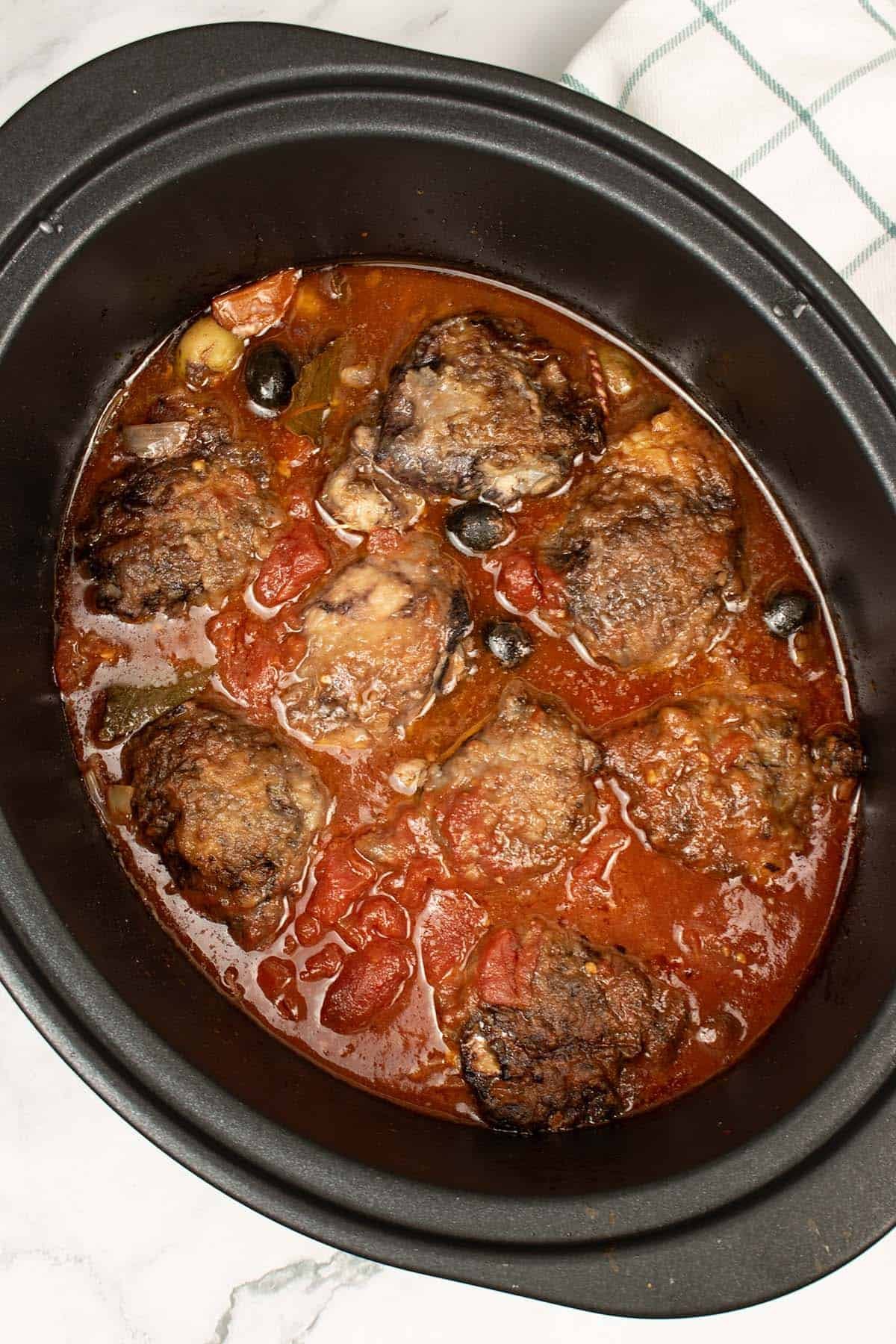 Slow cooker chicken cacciatore in the slow cooker pot with a teal and white checked towel on the side.