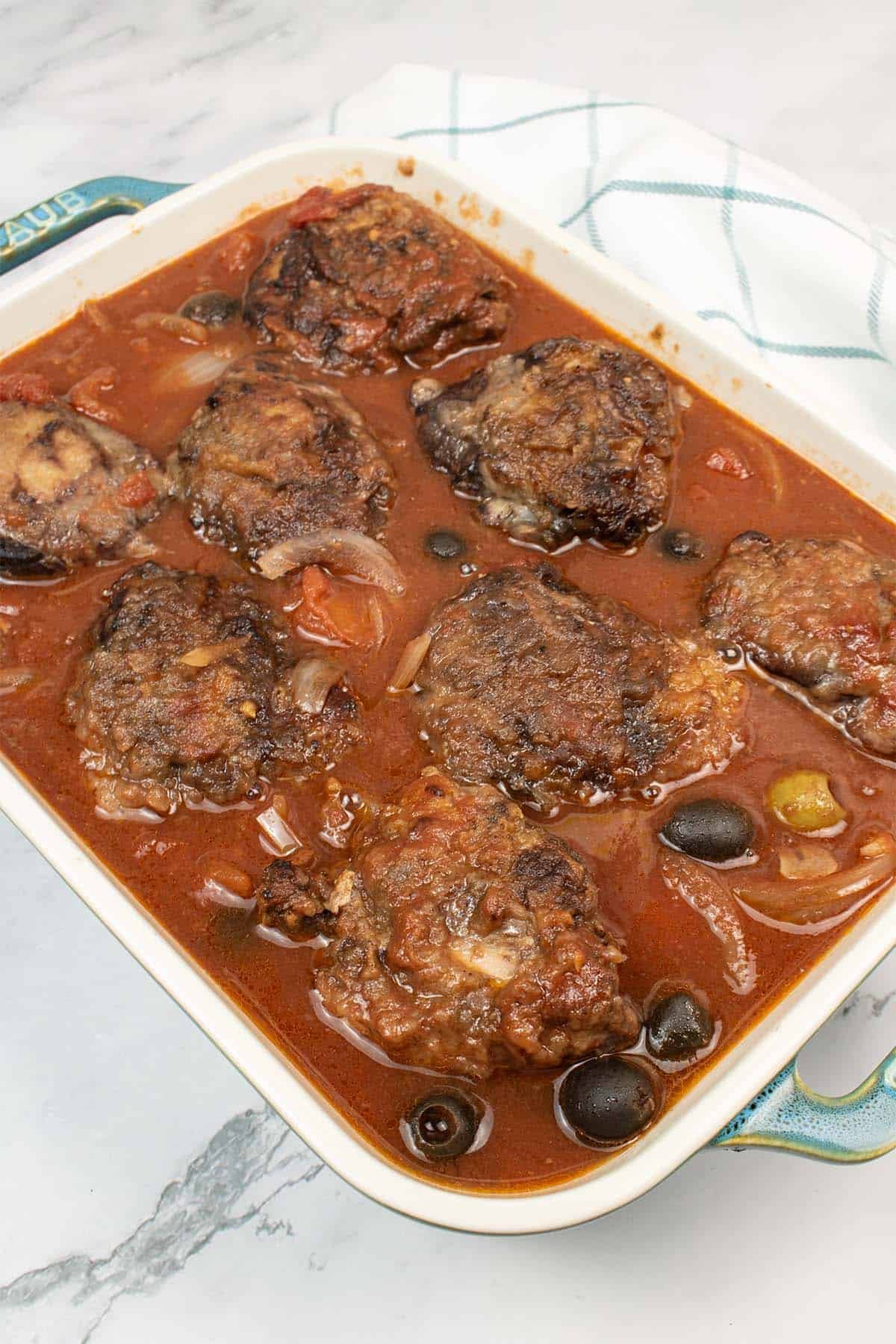 Slow cooker chicken cacciatore in a rectangle serving dish with a teal and white checked towel on the side.