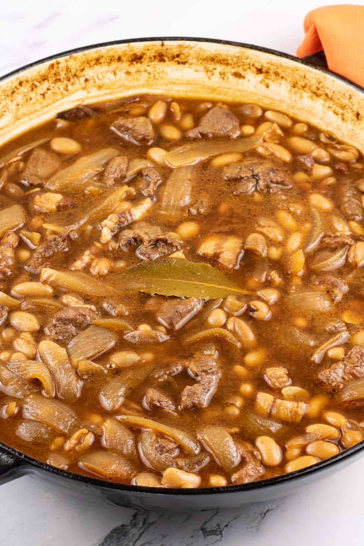 Beef and boston baked beans in large round casserole with orange napkin on the handle.