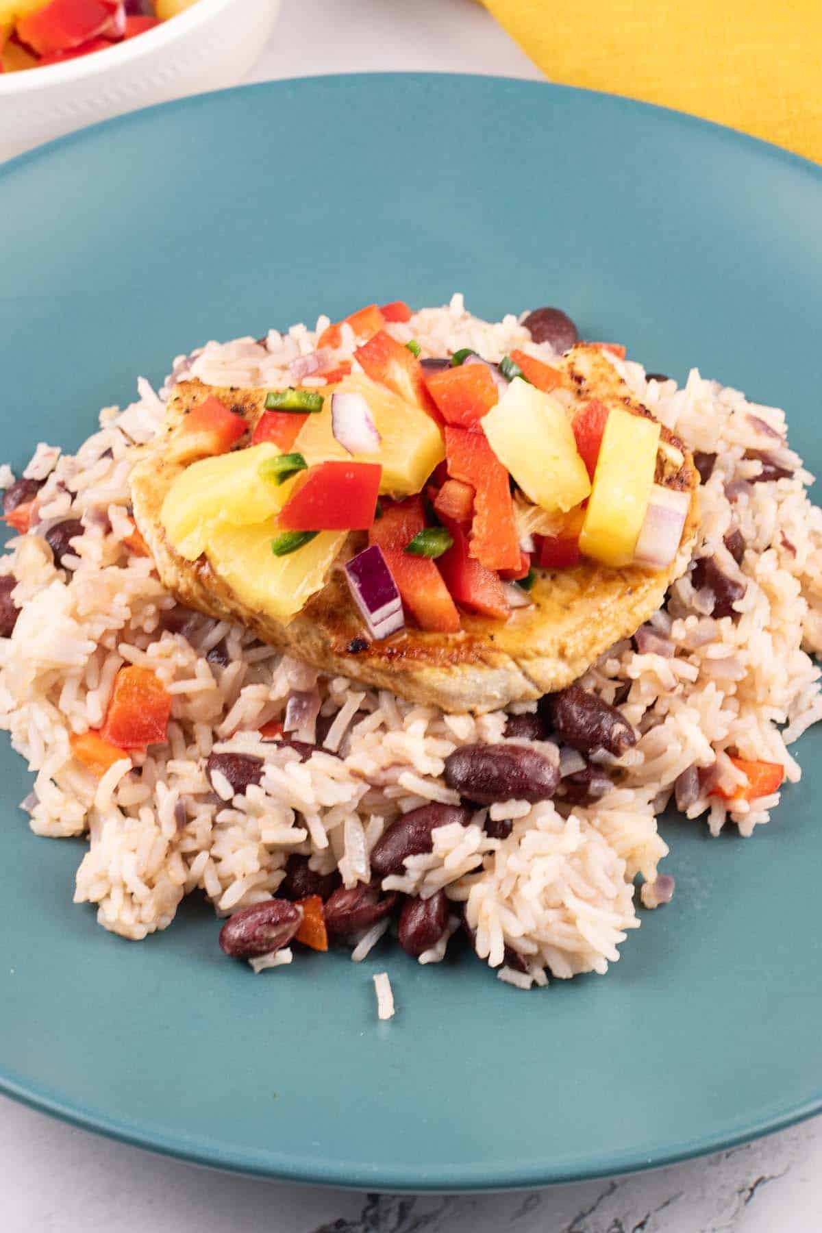 Cajun turkey steak with pineapple salsa and kidney bean rice on a teal plate. A bowl of salsa and mustard napkin on the side.