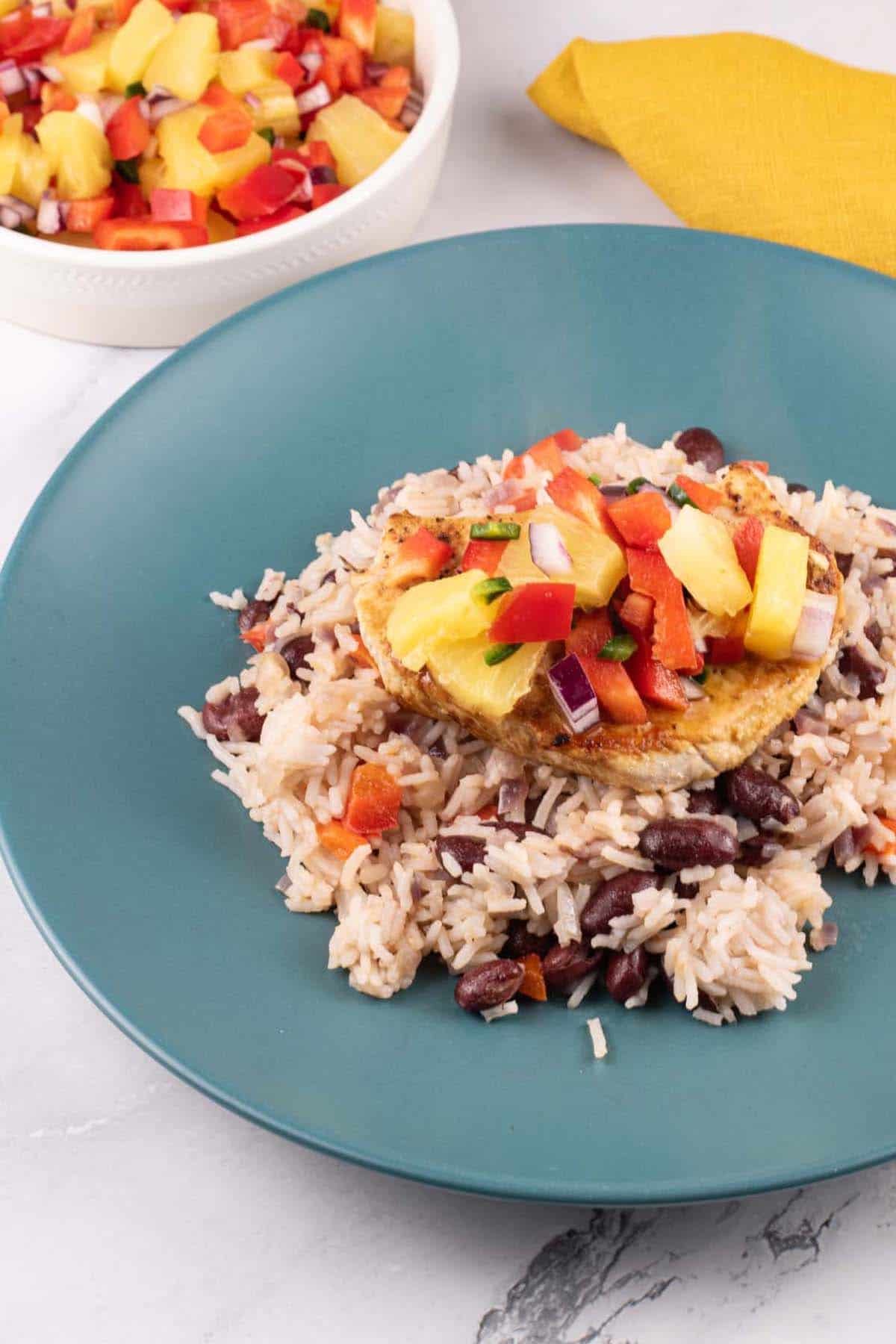 Cajun turkey steak with pineapple salsa and kidney bean rice on a teal plate. A bowl of salsa and mustard napkin on the side.