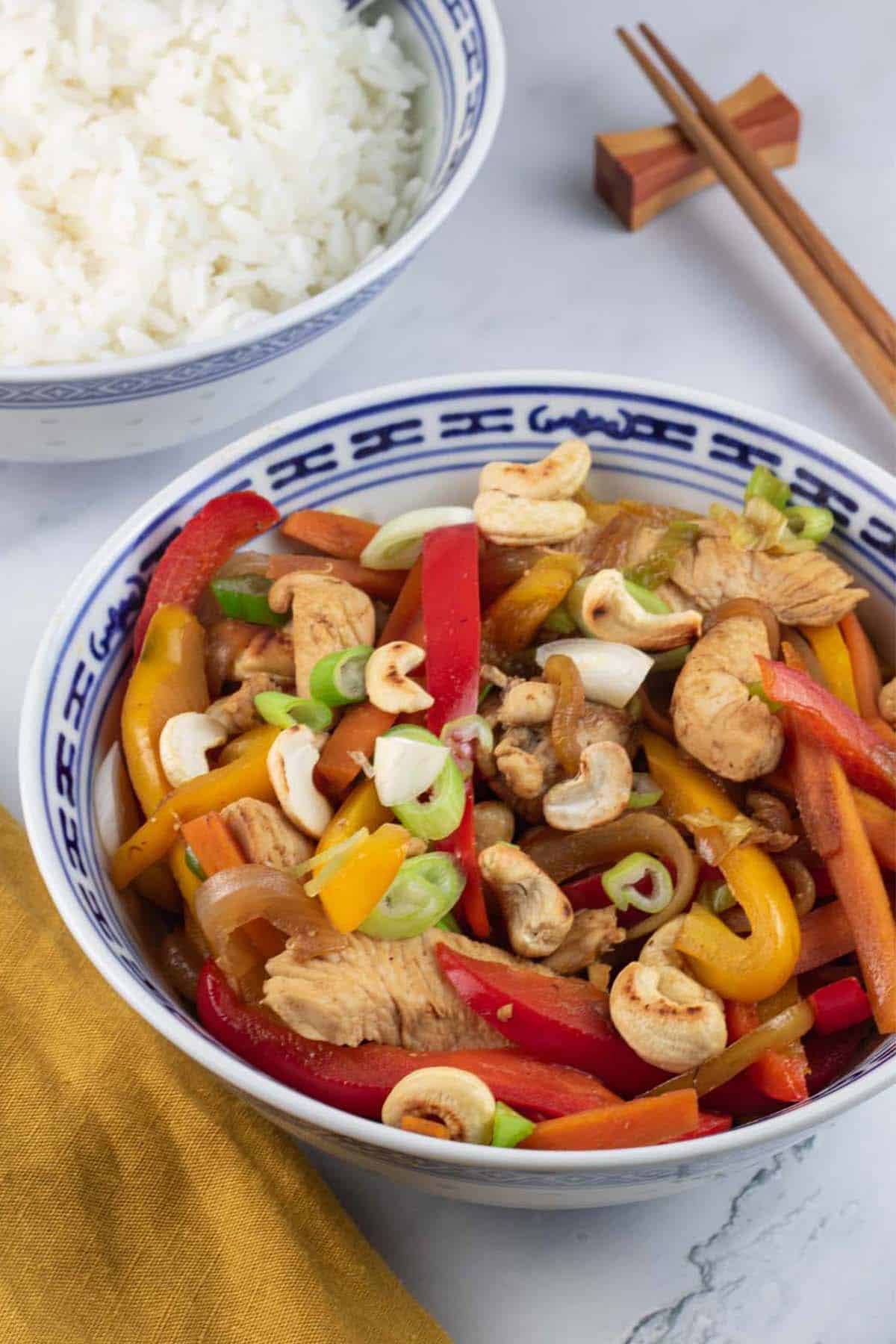 Chicken and cashew nut stir-fry in an oriental bowl with a bowl of jasmine rice and chopsticks on the side.