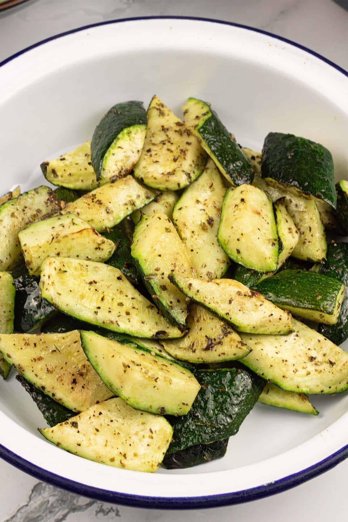 Close up of asy air fryer courgettes in a round blue rimmed white enamel dish.