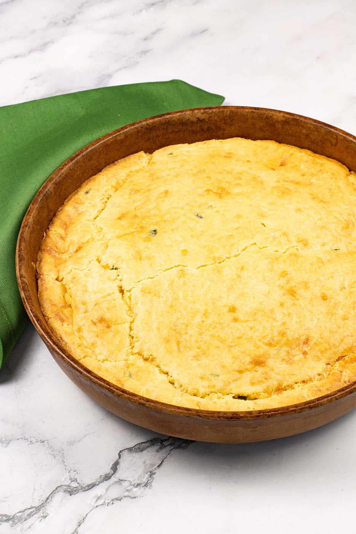 Easy homemade cornbread in a round stoneware dish with a green napkin on the side.