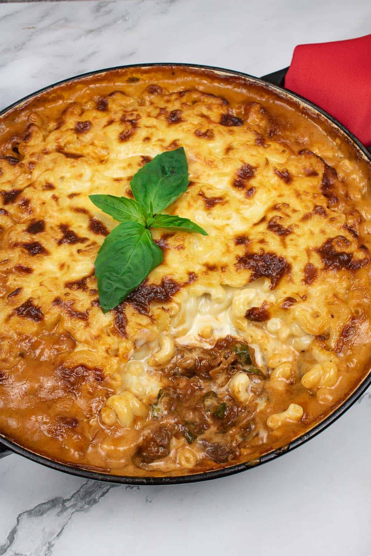 Mac 'n' cheese with rich beef ragu in a large round casserole with red napkin on the handle.