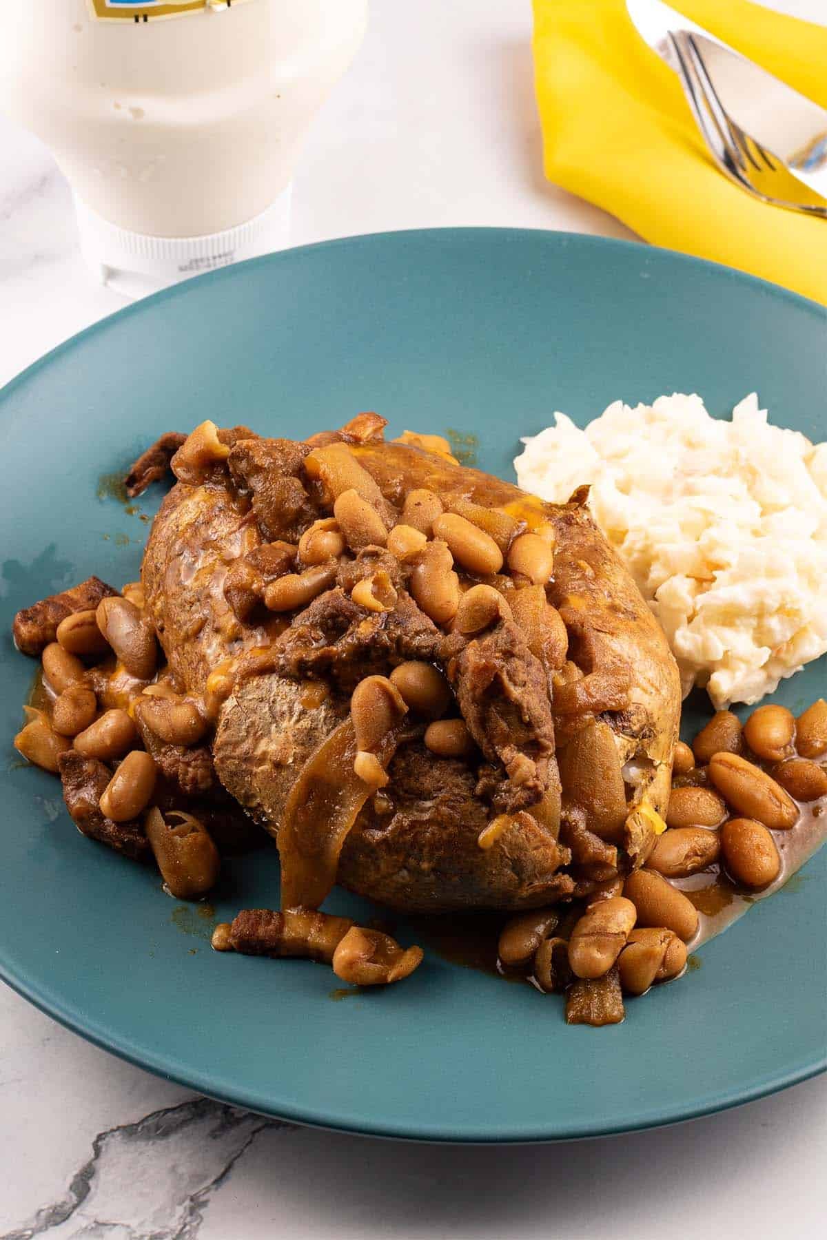 Perfect air fryer baked potato on a teal dinner plate topped with beef and Boston baked beans and coleslaw no the side.
