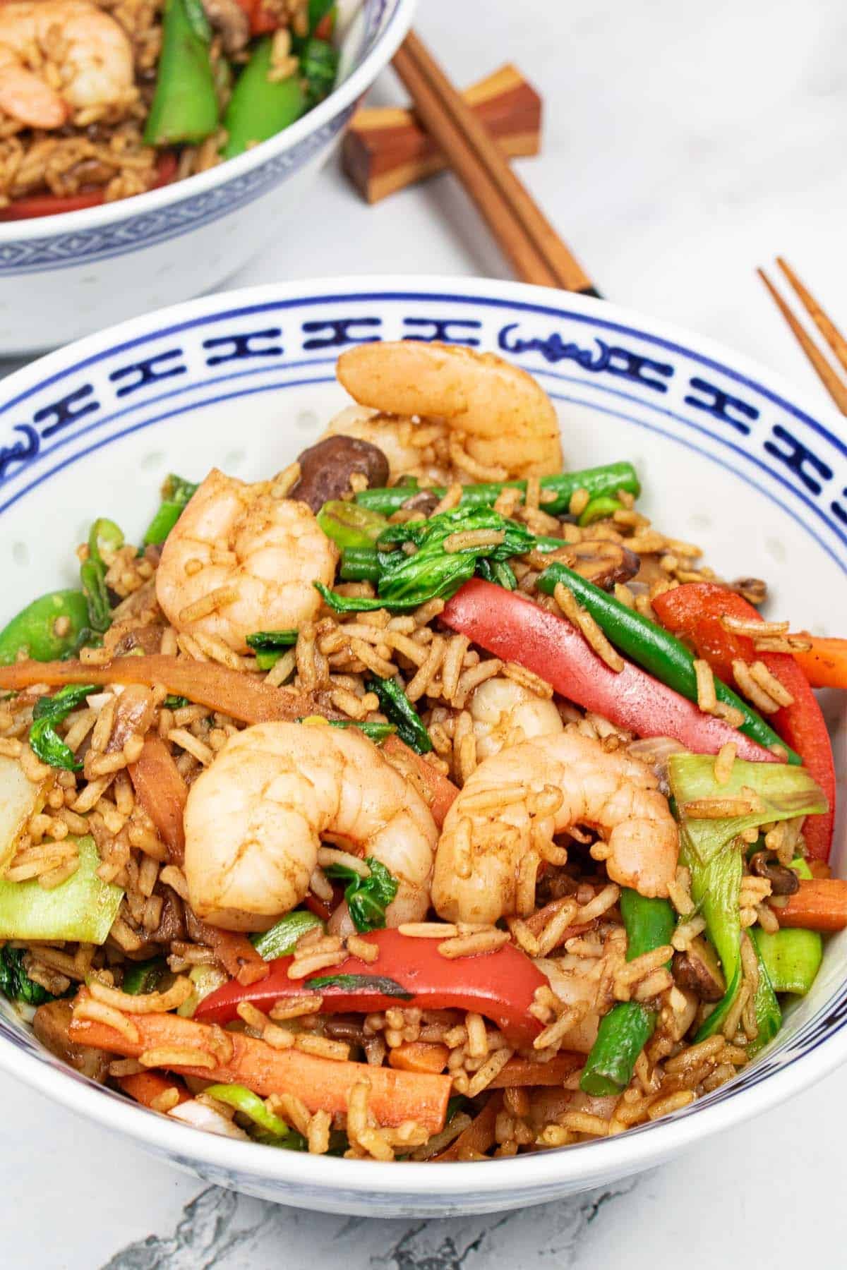 2 blue and white oriental bowls of prawn and vegetable fried rice with chopsticks on the side.