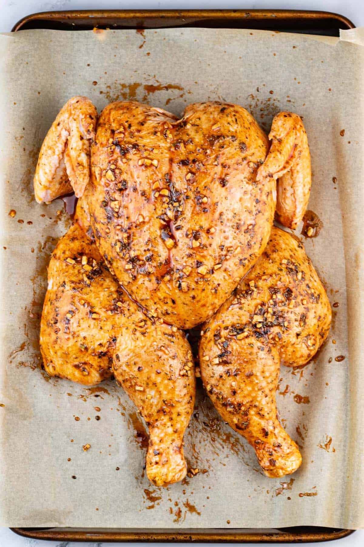 Uncooked Spanish spatchcock chicken on a large baking tray.