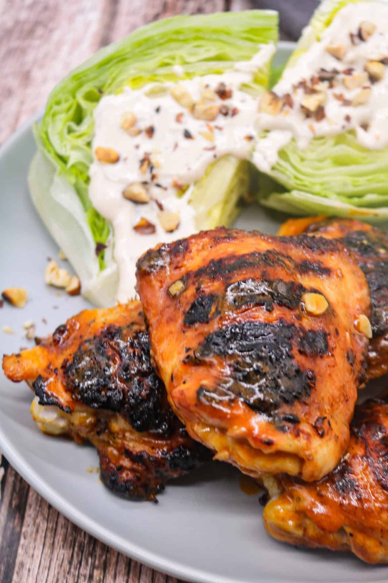 BBQ buffalo chicken thighs with wedged ranch salad on a grey dinner plate.