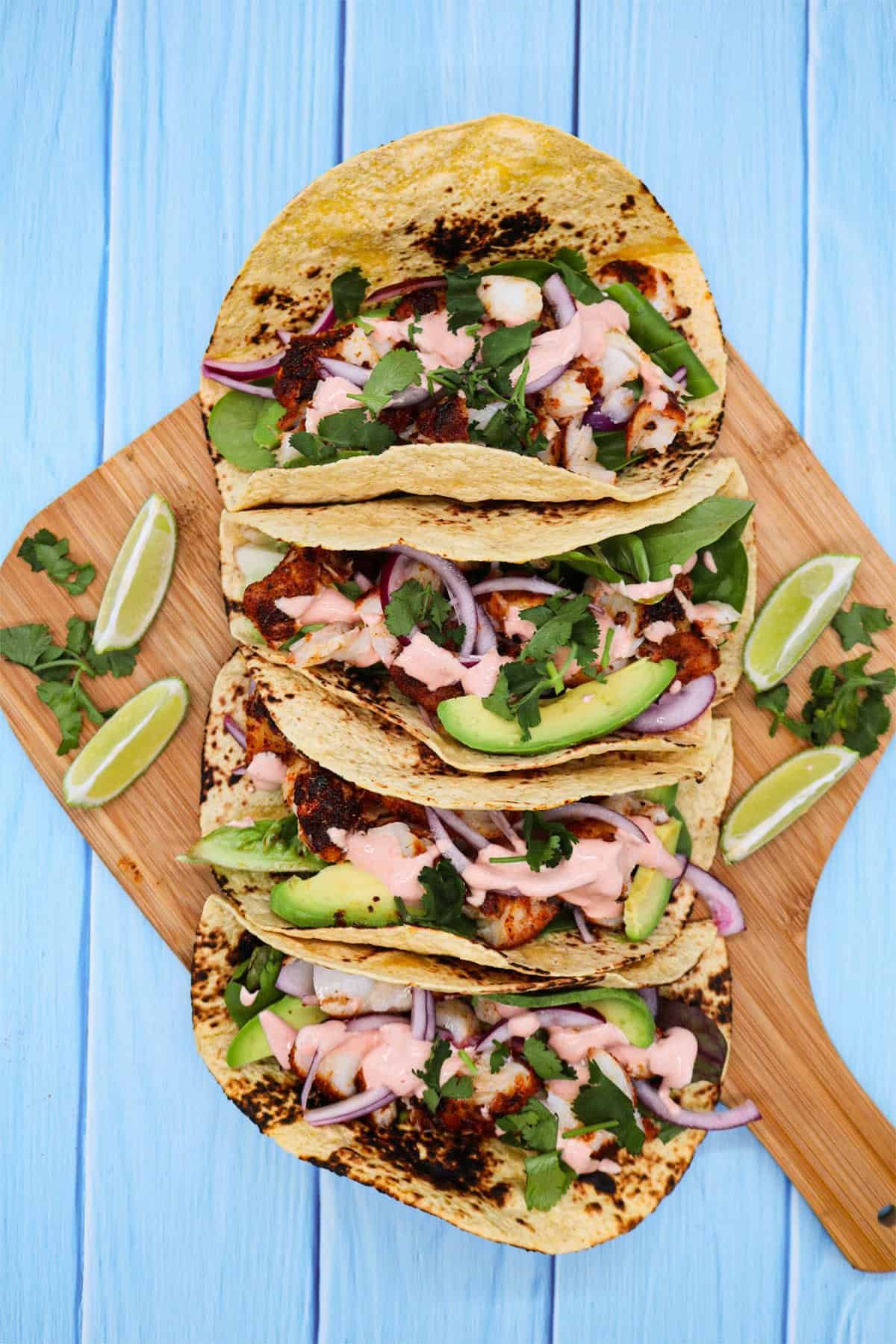 Blackened cod tacos on a wooden board with lime wedges on the side.