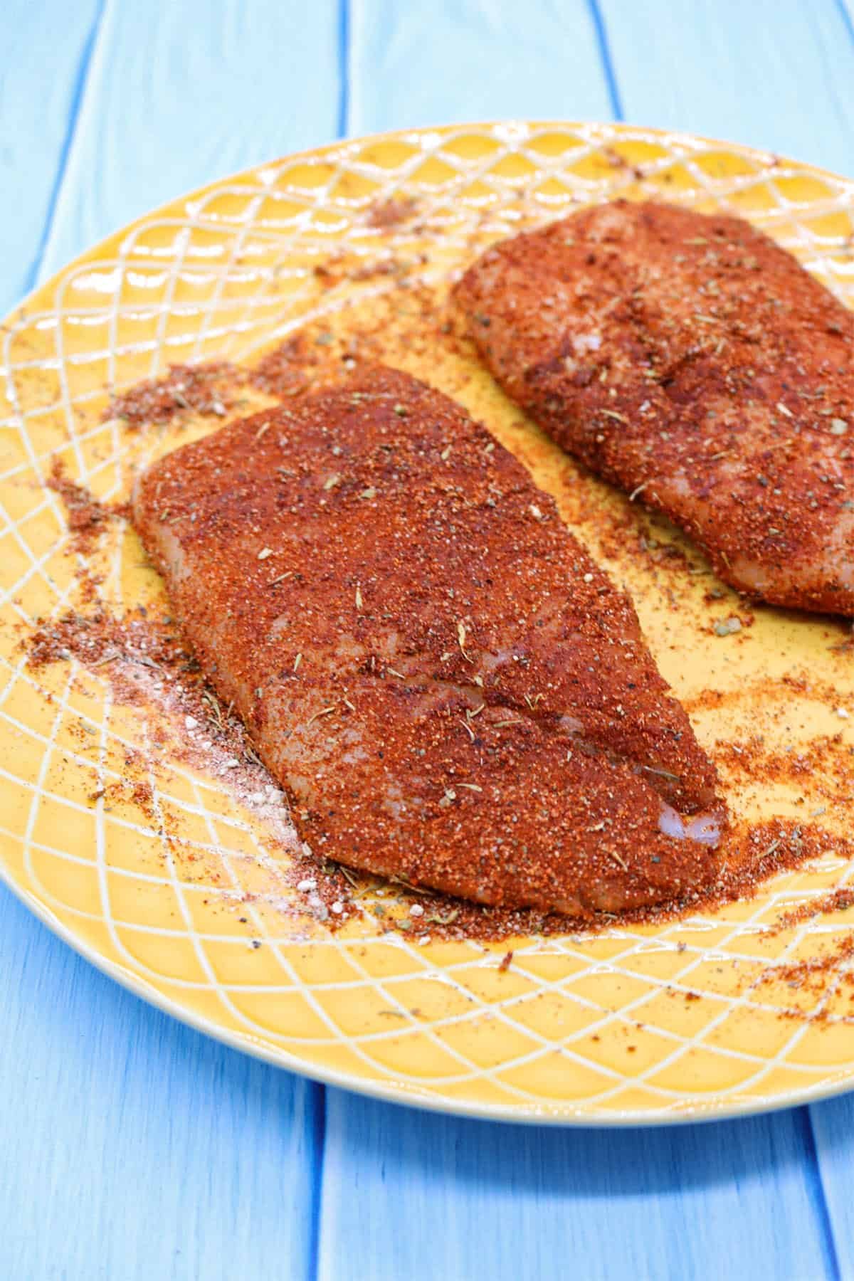 Raw cod pieces coated in the seasoning, on a yellow plate.