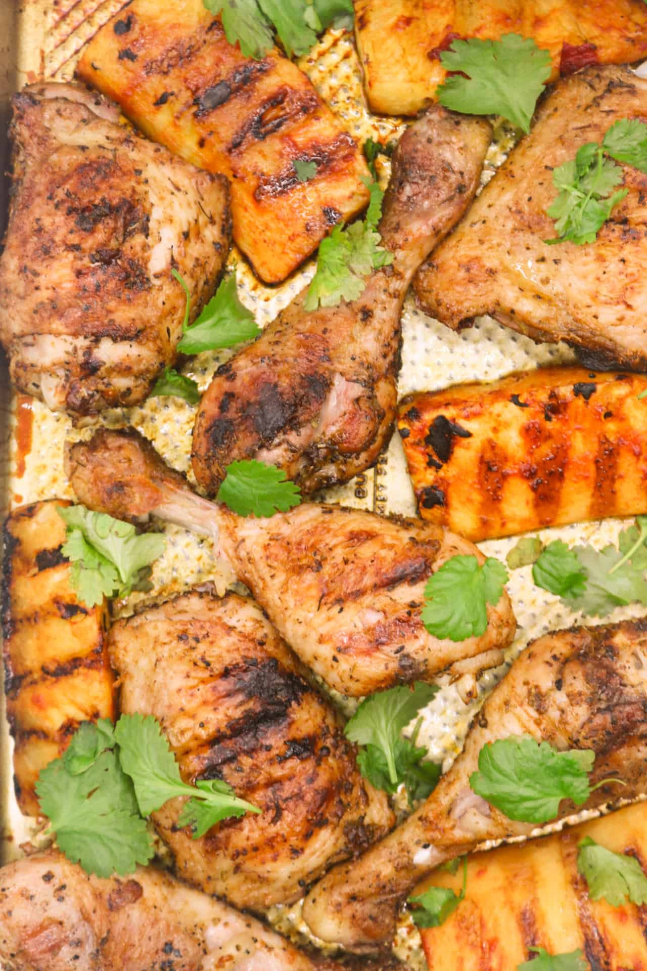 Cajun chicken with charred pineapple wedges on a large baking tray, garnished with coriander.