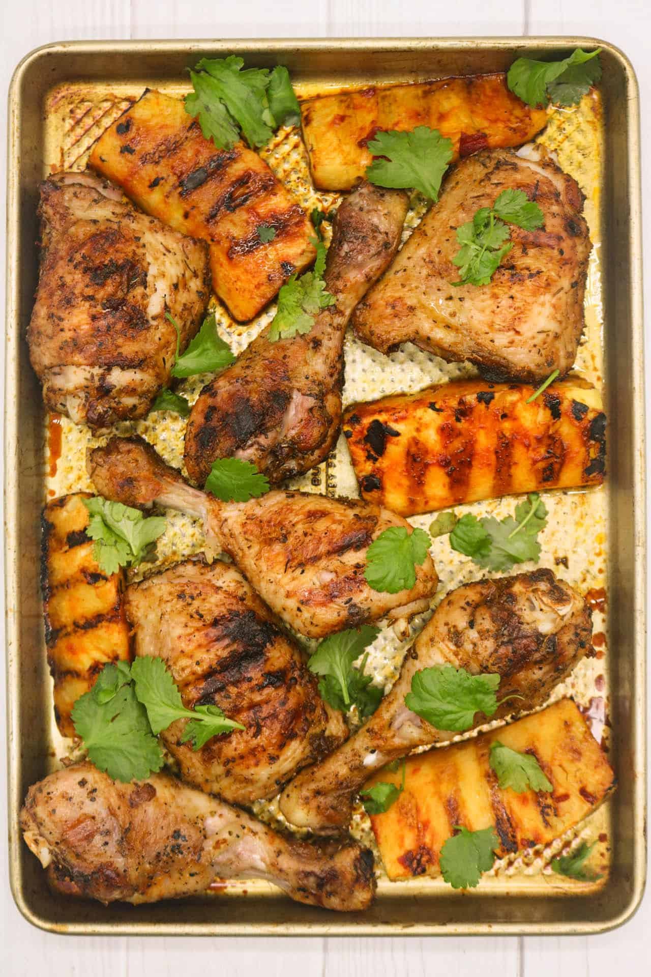 Cajun chicken with charred pineapple wedges on a large baking tray, garnished with coriander.