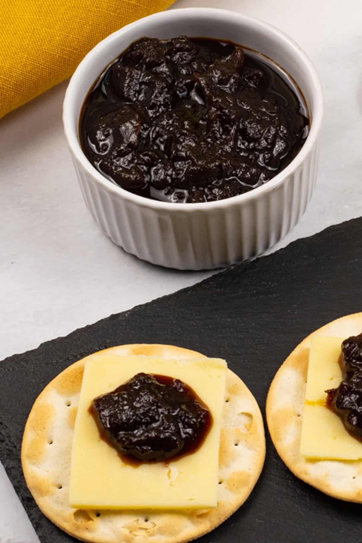 Caramelised red onion chutney made in the Thermomix in a white ramekin with crackers, cheese and chutney on a black slate.