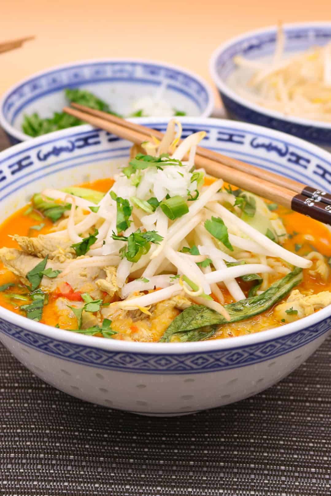 Chiang mai noodles made in the Thermomix in an oriental bowl with chopsticks and bowls of beansprouts, coriander and spring onions in the background.
