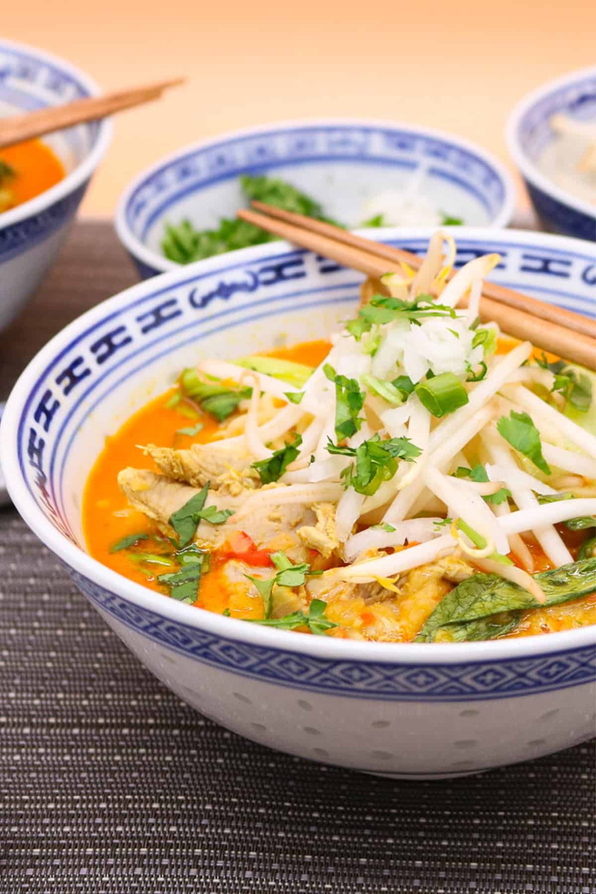 Chiang mai noodles made in the Thermomix in an oriental bowl with chopsticks and bowls of beansprouts, coriander and spring onions in the background.