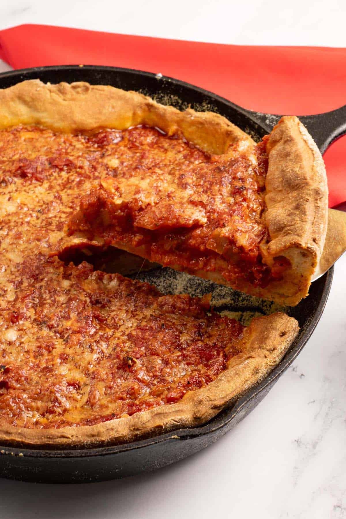 Chicago deep pan pizza in a black skillet with a slice being held up and a red napkin on the side.