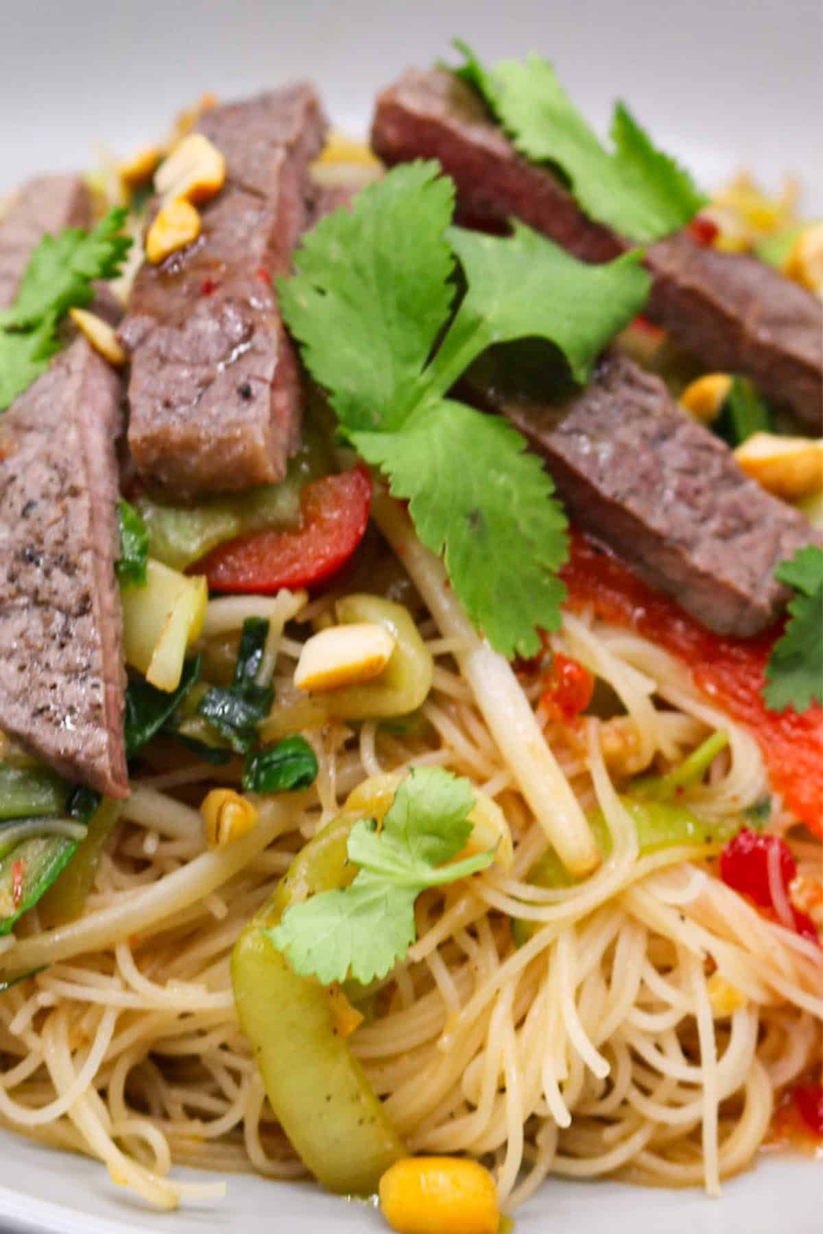 Close up of chilli beef and vegetable rice noodles with peanuts in a grey bowl.
