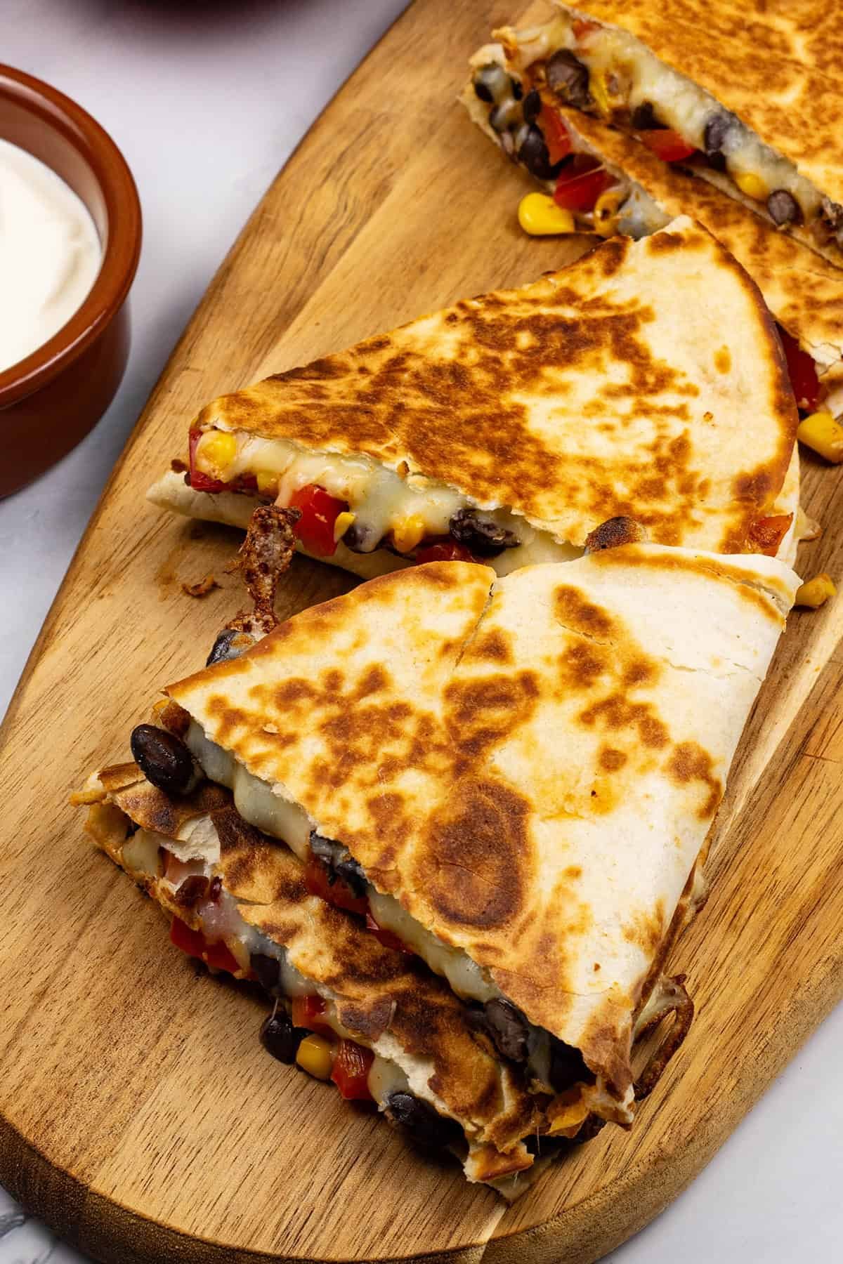 Close up of chipotle black bean and corn quesadillas on a board with a dish sour cream on the side.