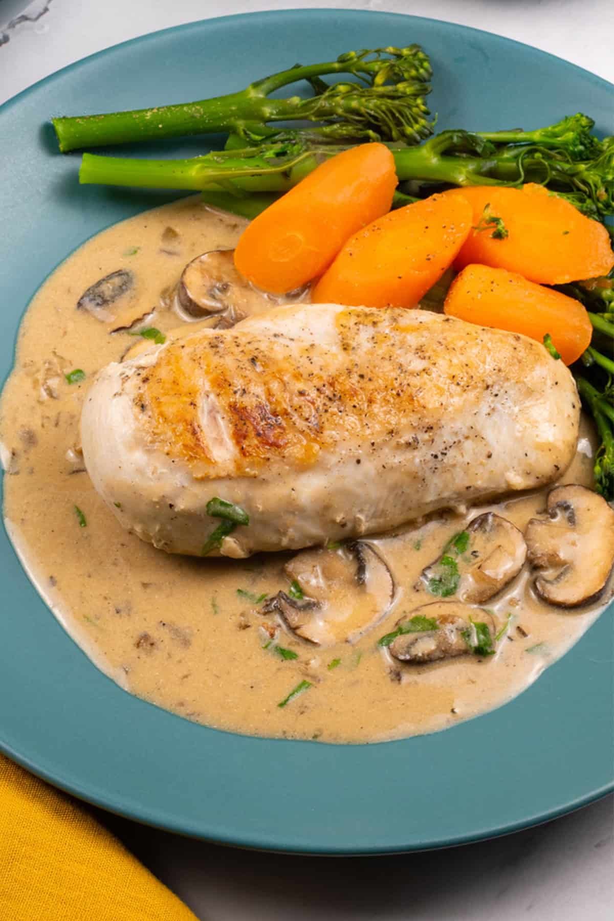 A portion of creamy mushroom chicken with broccoli and carrots on a teal dinner plate.