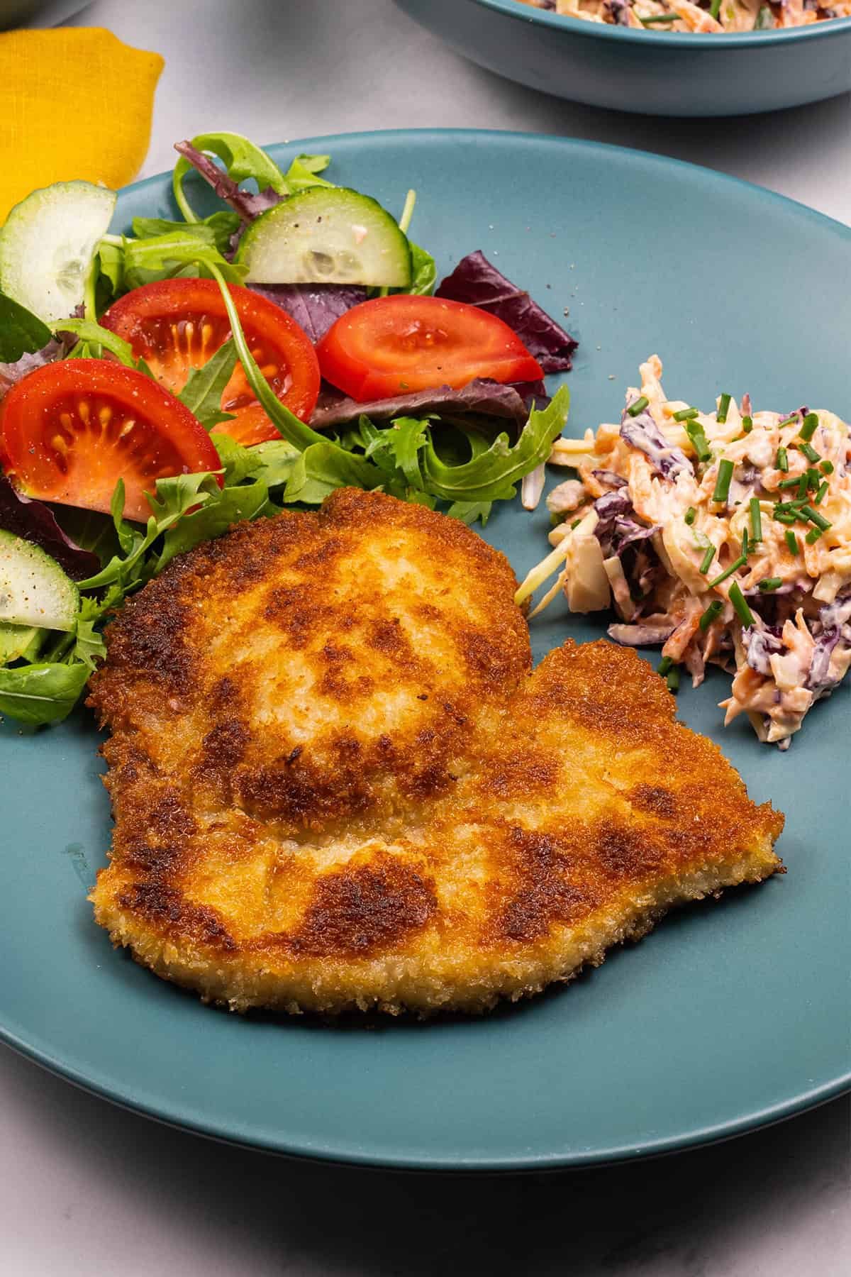 A crispy pork schnitzel, coleslaw and salad on a teal dinner plate.