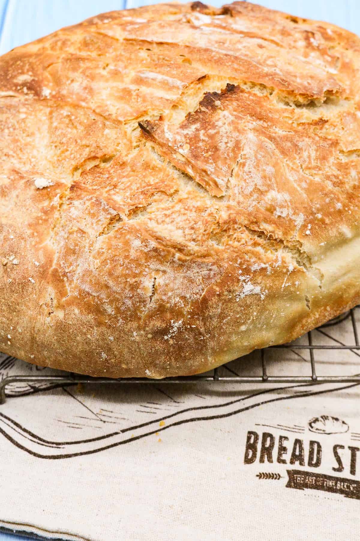 Crusty bread on a cooling rack sitting on top of a cloth bread bag.