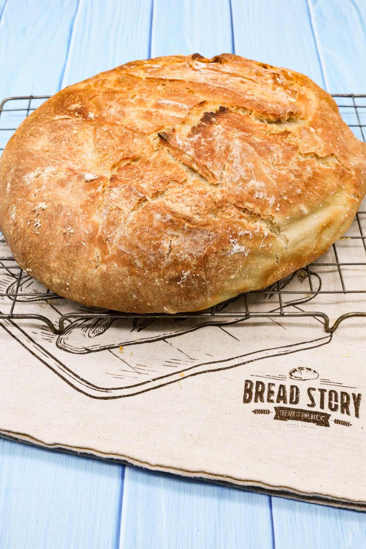 Crusty bread on a cooling rack sitting on top of a cloth bread bag.