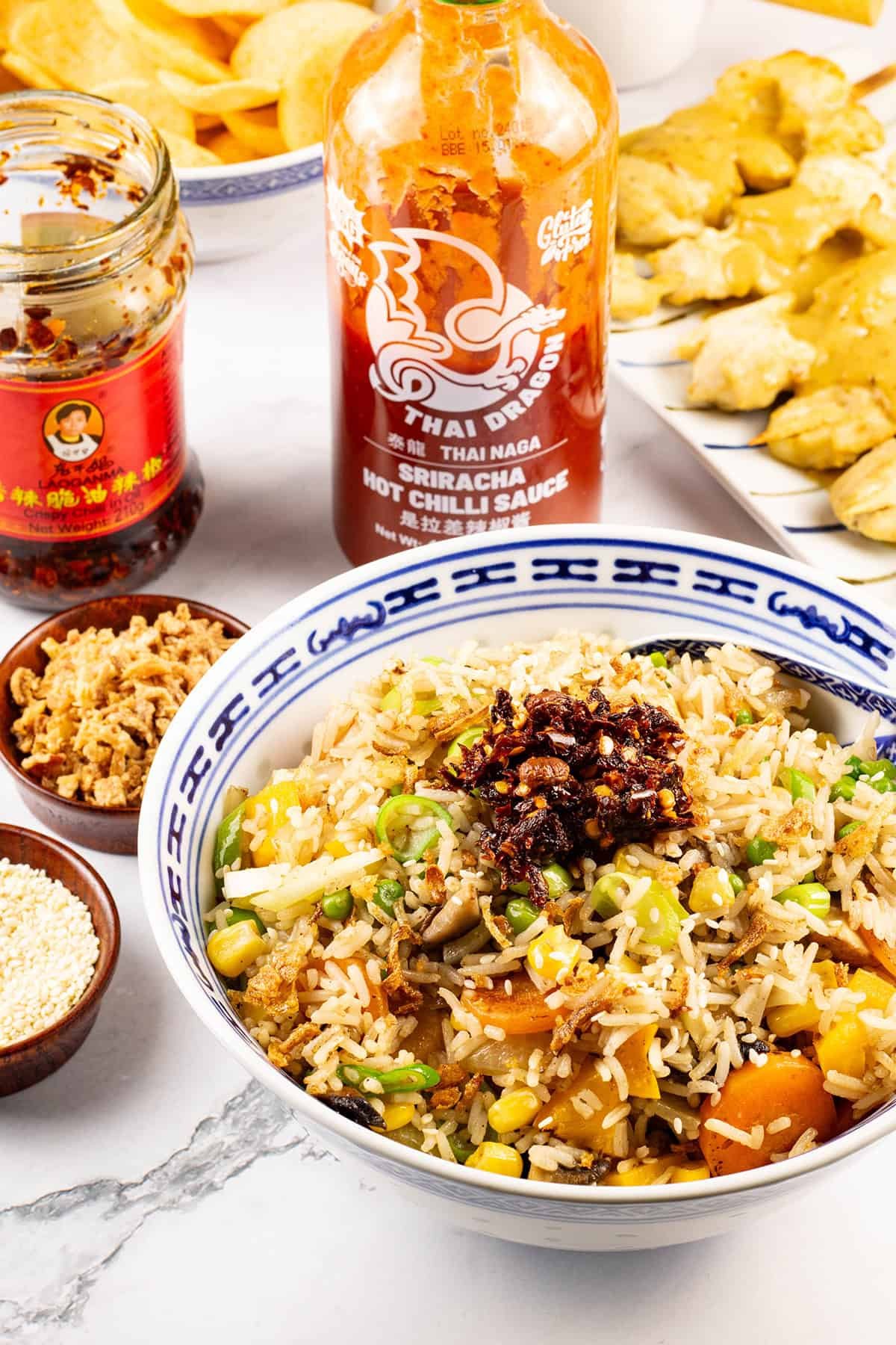 Easy vegetable fried rice in a blue and white oriental serving bowl with spoon and Asian condiments on the side.