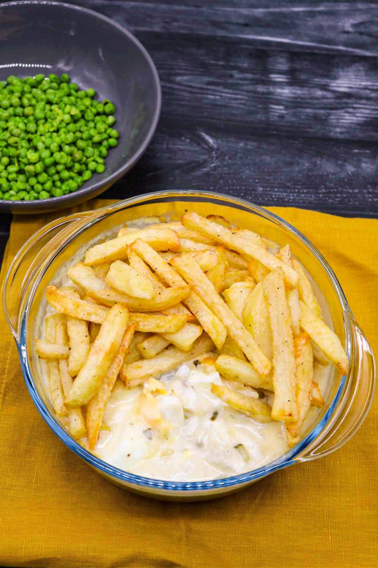 Fish and chip pie in a round glass serving bowl plus a bowl of peas on the side