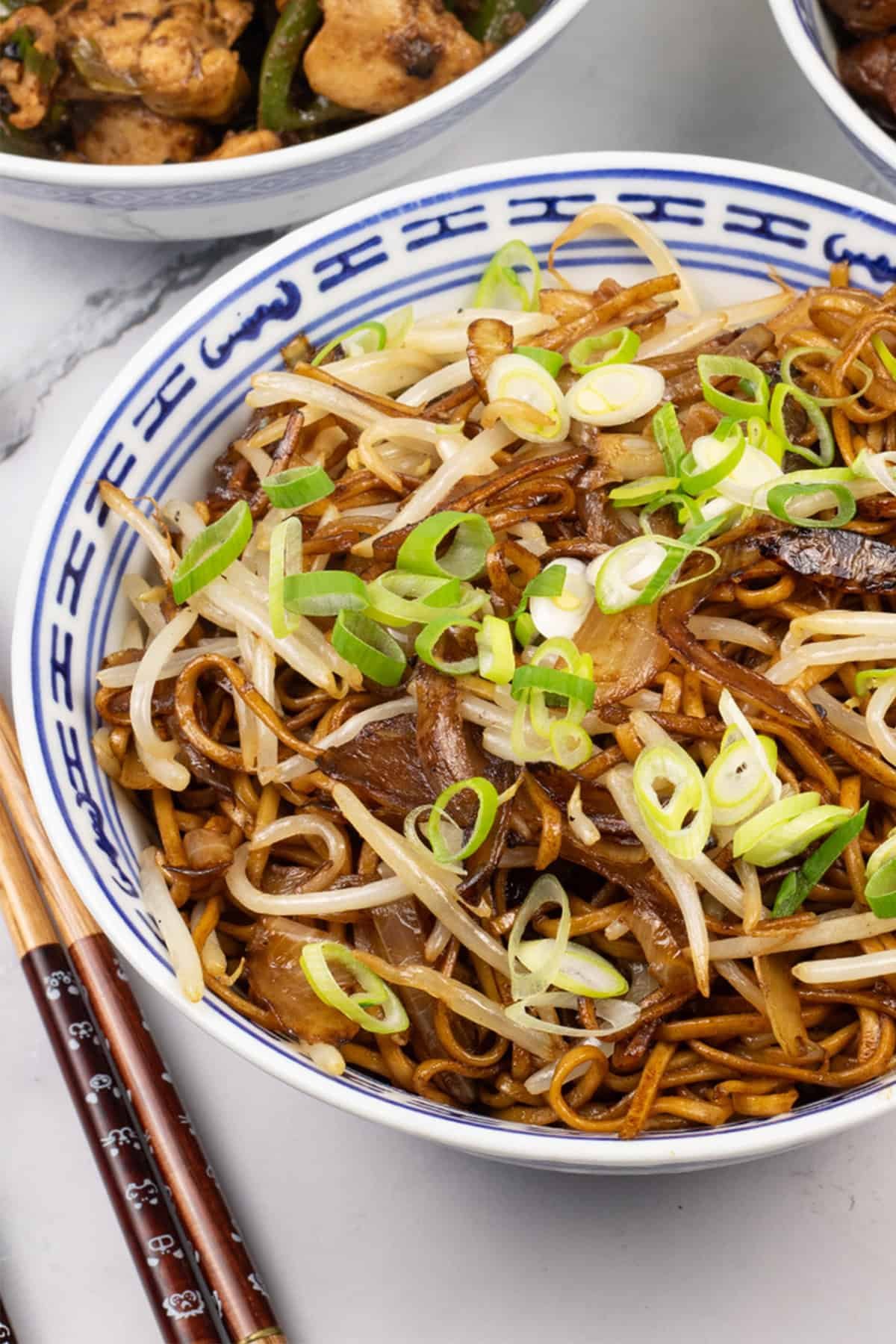 Close up of fried noodles with beansprouts in an oriental bowl with chopsticks on the side.