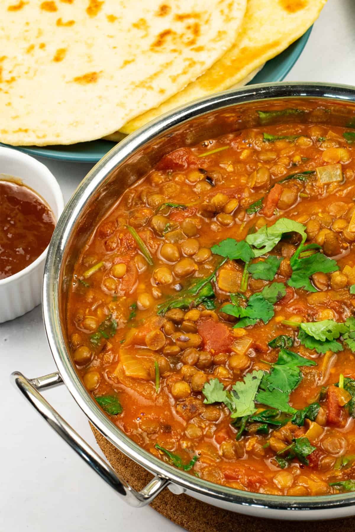 Green lentil dal in a balti dish with a plate of quick naan breads and small dish of mango chutney on the side.