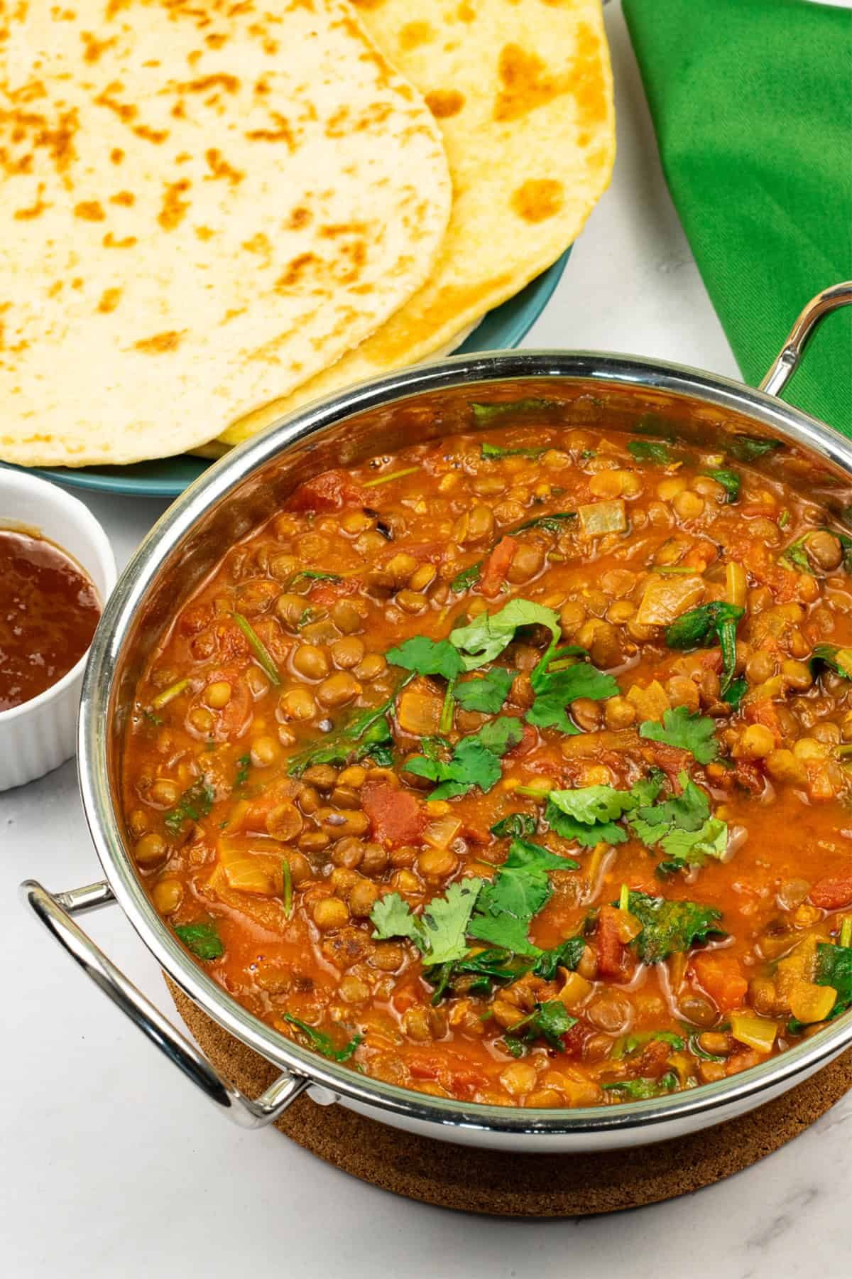 Green lentil dal in a balti dish with a plate of quick naan breads and small dish of mango chutney on the side.