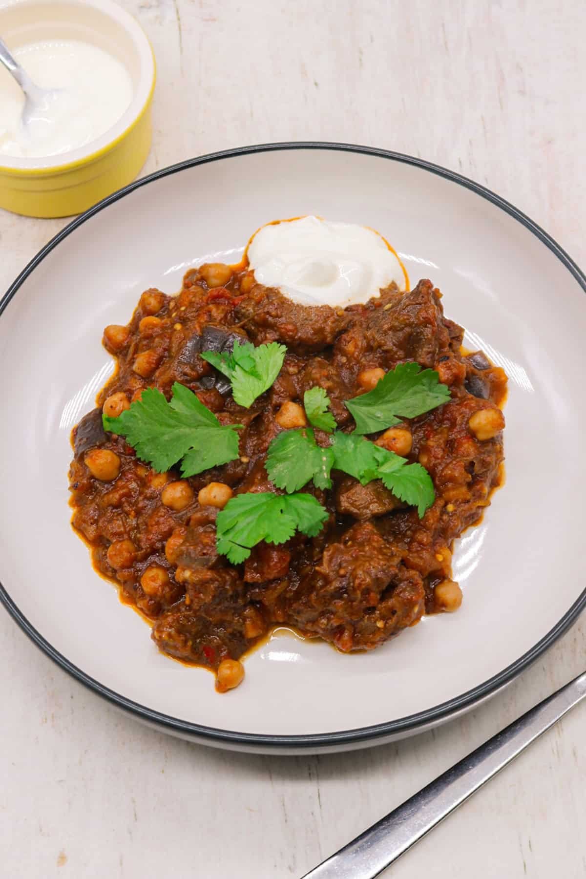 Harissa beef stew in a bowl garnished with coriander and sour cream on the side.
