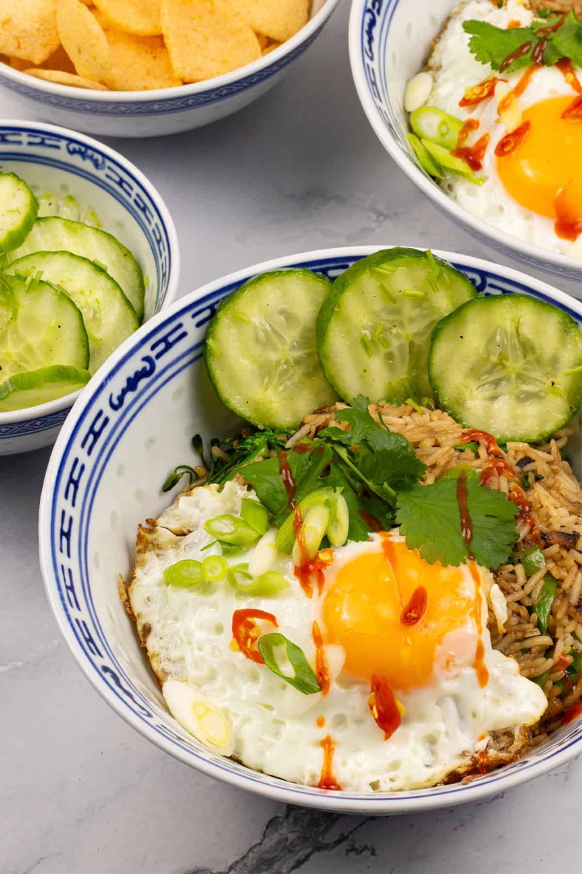 2 portions of nasi goreng in oriental bowls with bowls of cucumber pickle and Thai prawn crackers on the side.