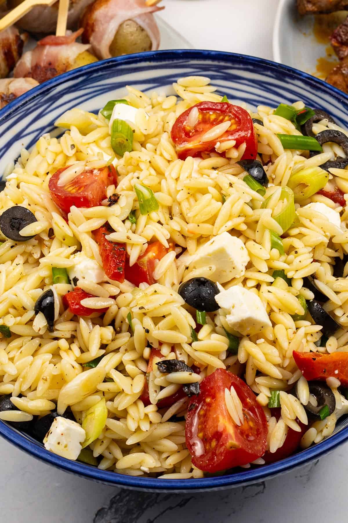 Orzo salad with feta in a blue and white striped bowl.
