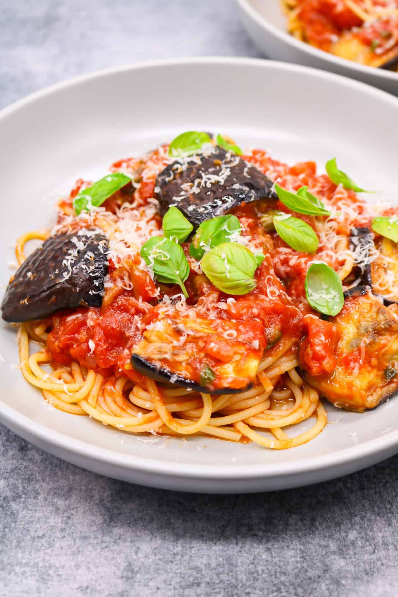 2 grey bowls of pasta all norma garnished with basil leaves and grated parmesan.