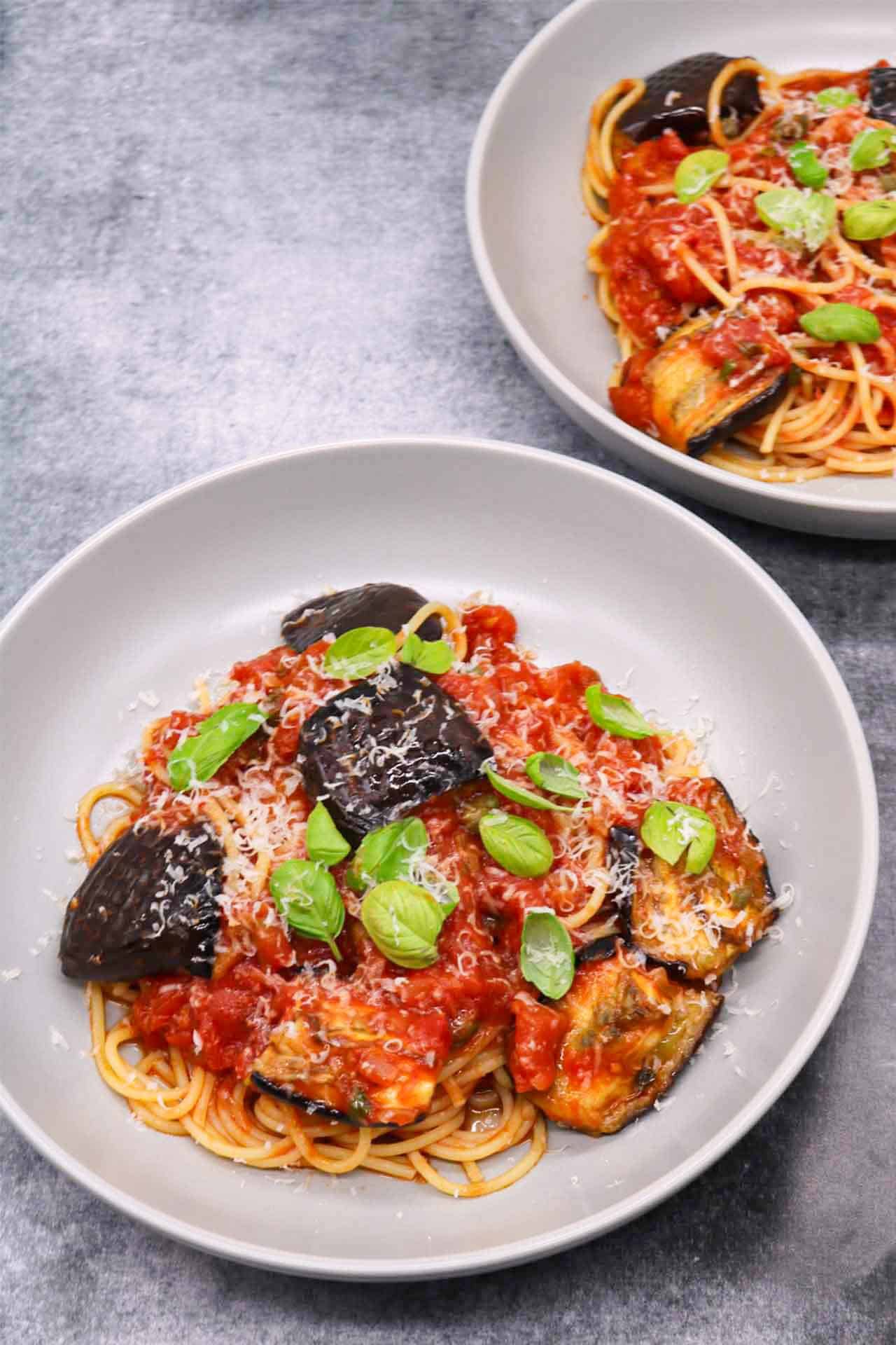 2 grey bowls of pasta all norma garnished with basil leaves and grated parmesan.