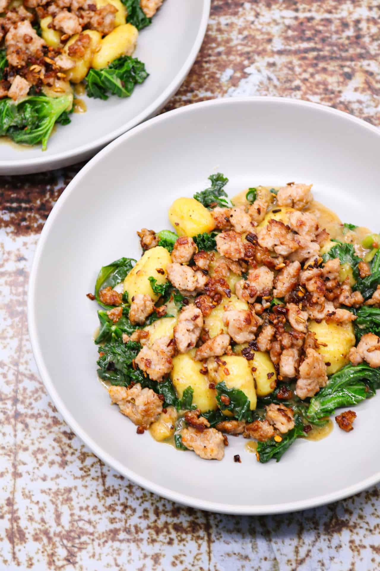Two grey bowls of sausage, kale and gnocchi one pot.