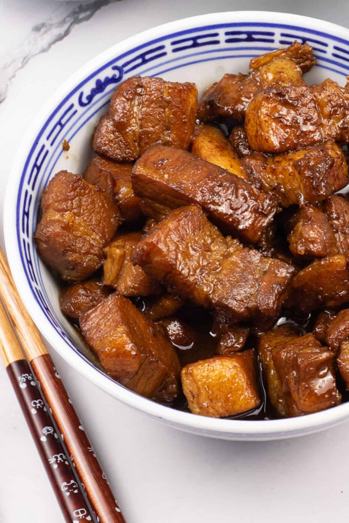 Shanghai-style braised pork belly in an oriental bowl with chopsticks on the side.