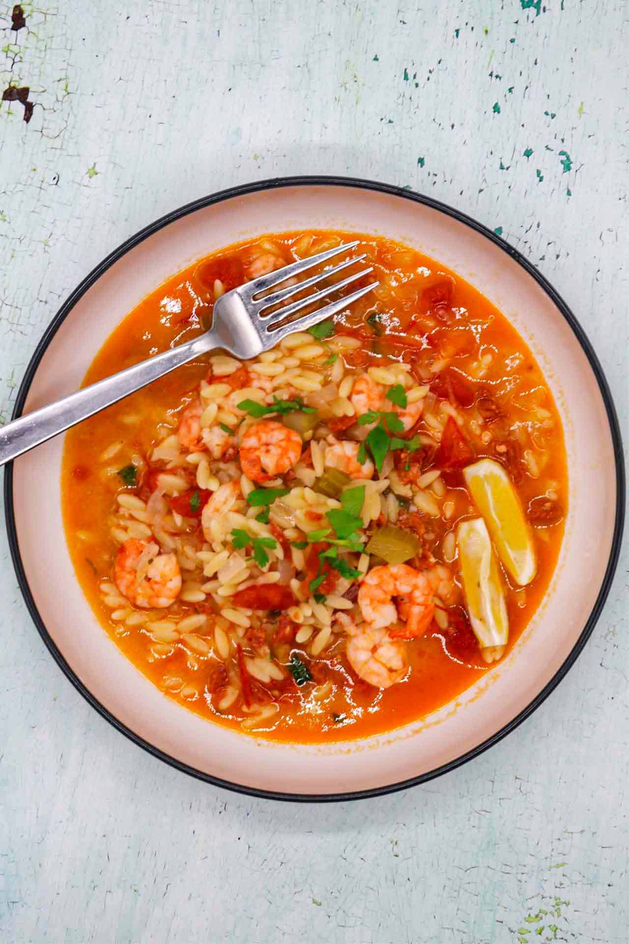 Slow cooker prawn and chorizo paella in bowl with lemon wedges and a fork