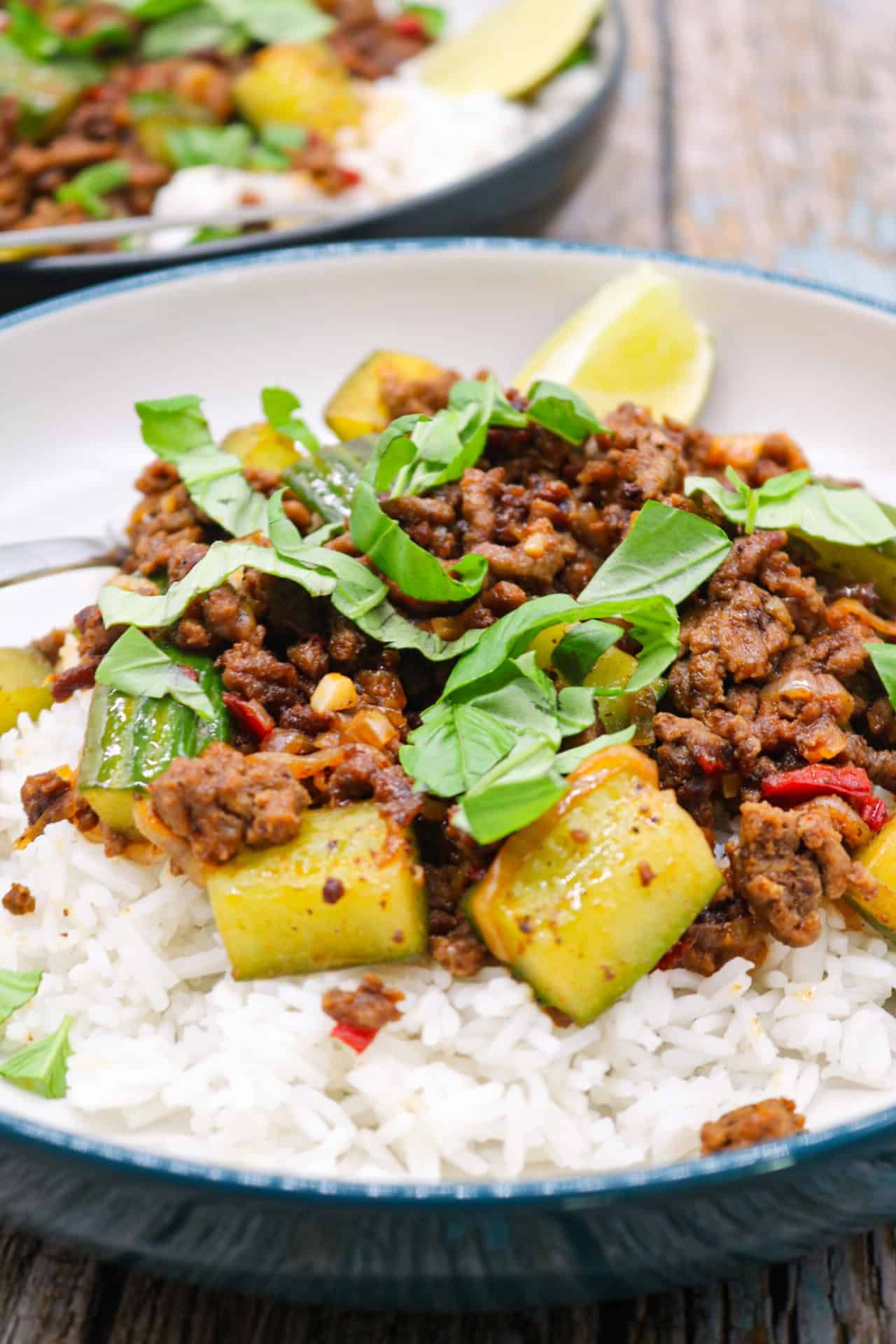 Two bowls of spicy beef and crushed cucumber stir-fry served on rice with forks and lime wedges.