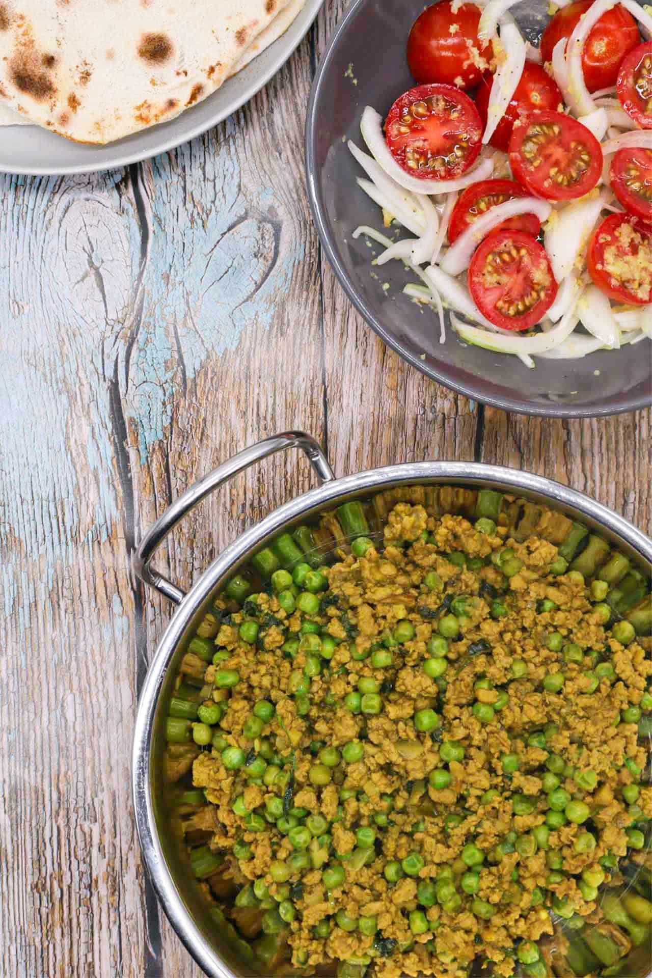Turkey keema curry in a balti dish with a plate of naan and bowl of tomato and onion salad on the side.